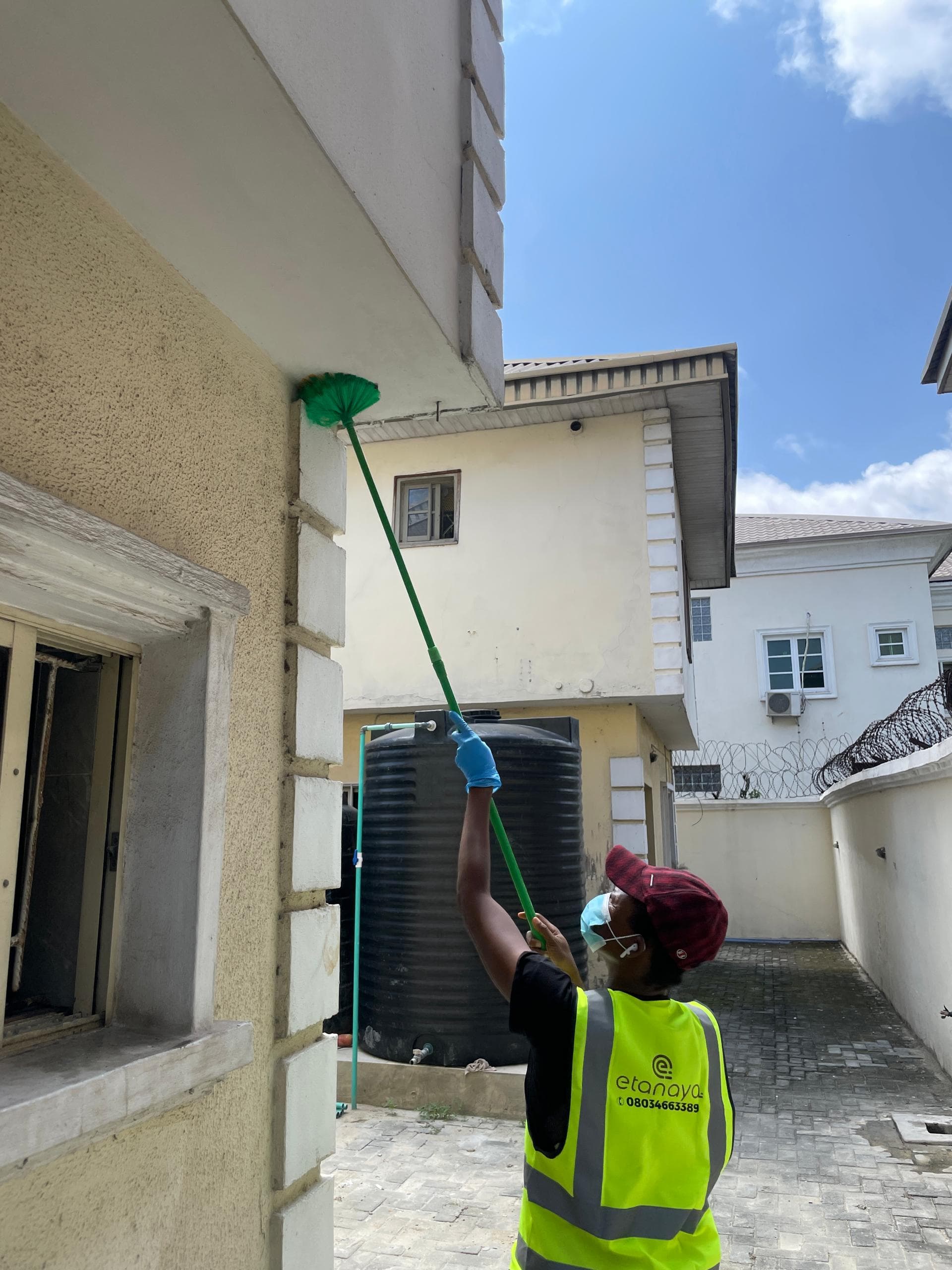 Etanaya operative using an extendable duster to reach a high exterior soffit